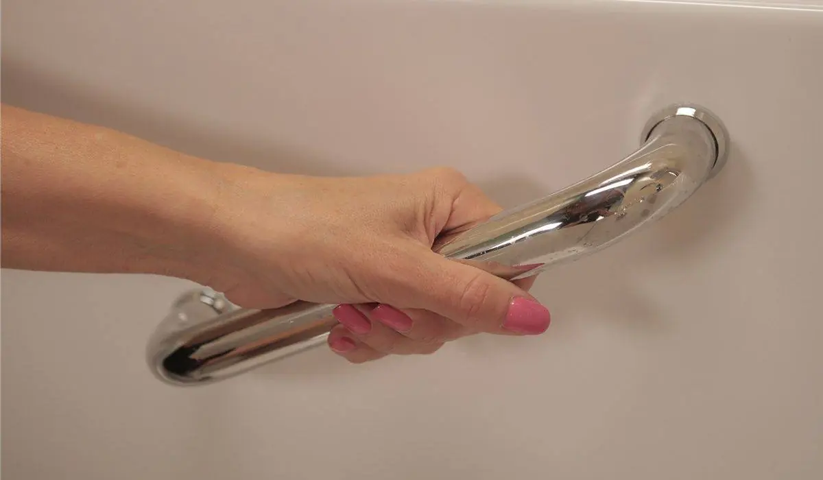 Hand holding a chrome grab bar on the side of a walk-in tub in an accessible bathroom