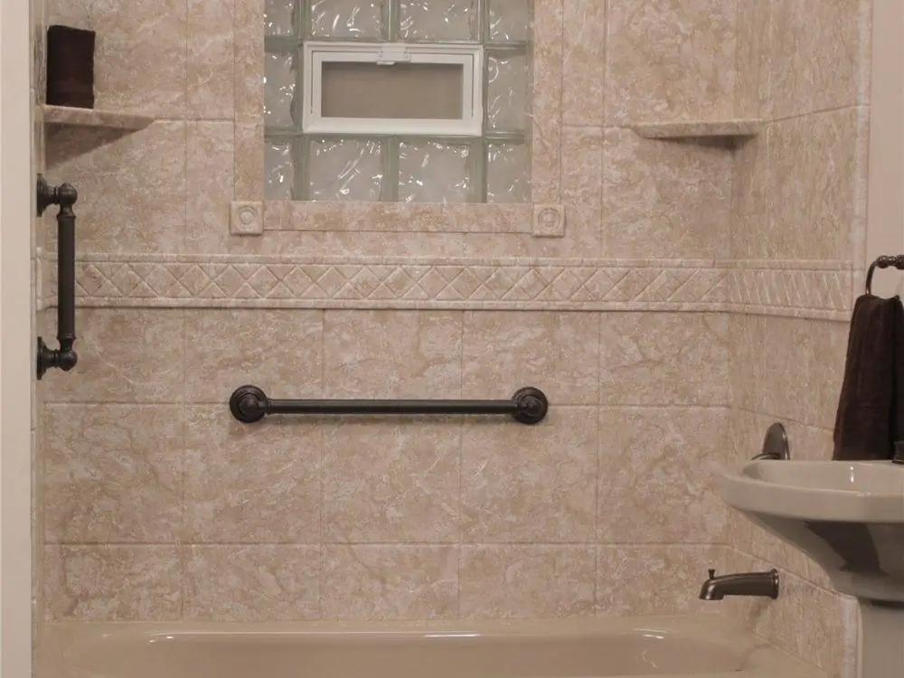 Stone look tub surround with two bronze grab bars below a glass block window