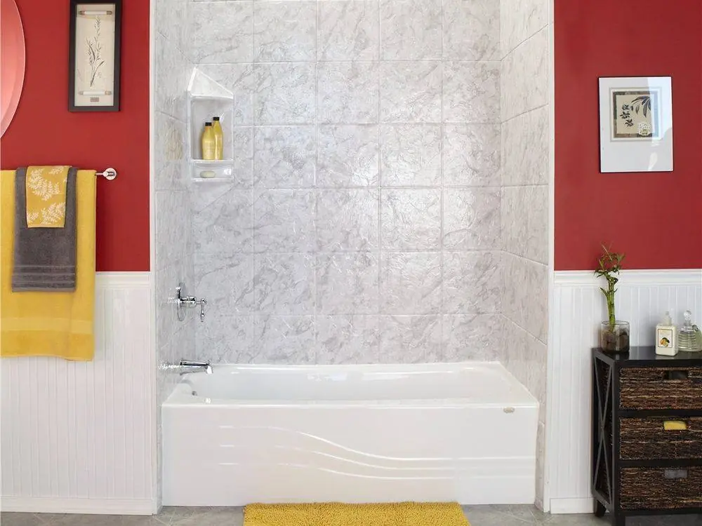 White bathtub with a light gray stone look surround, a white wainscot and red walls