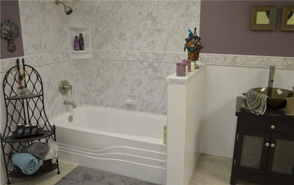 New white bathtub with a marble look surround, a decorative border and a beadboard half wall