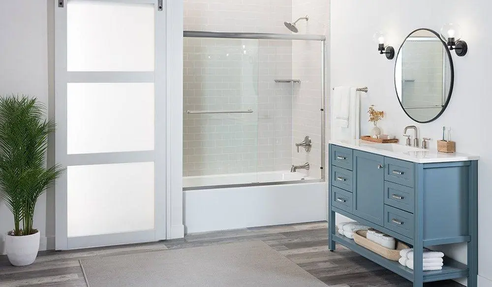 Bathroom with a sliding barn door, a tub with glass doors and a blue vanity