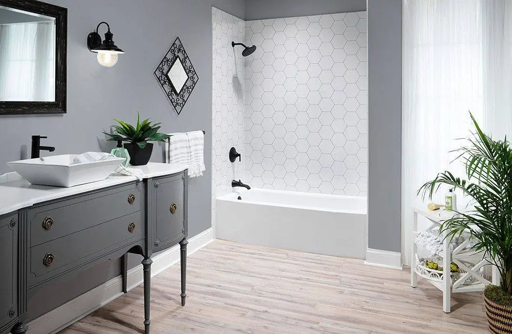 White bathtub with a white hexagon tile look wall surround and a matte black fixture in a grey bathroom