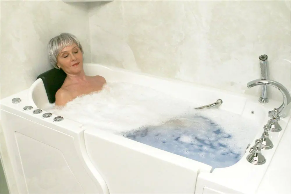 Woman relaxing in a bubble filled walk-in tub with jet buttons and a handheld shower on the rim