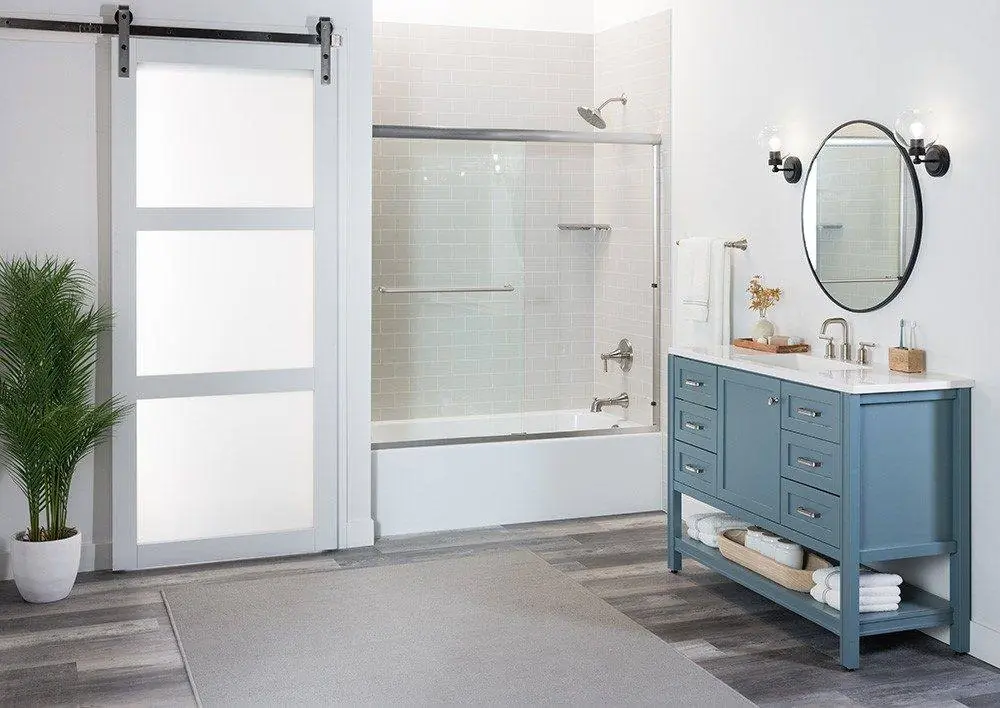 Tub and shower combo with a sliding glass shower door, light subway tile look walls and a blue vanity