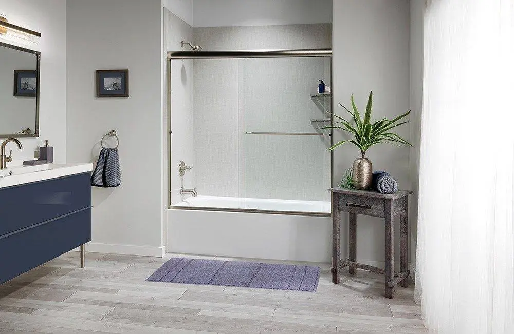Bathtub with a brushed nickel framed sliding glass door, light grey walls and a navy vanity