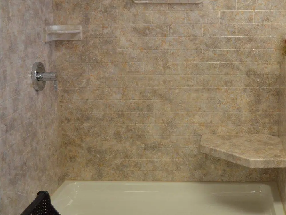 Shower with tan stone look wall panels in a brick pattern, a corner seat and a soap dish