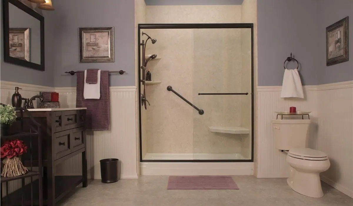 Remodeled shower with a bronze framed sliding glass door, cream stone look walls, a grab bar and a corner seat