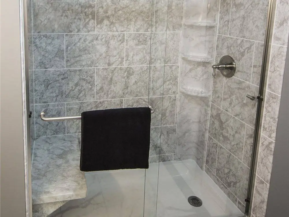 Grey marble look shower walls with a bench seat, a grab bar and a brushed nickel framed glass door