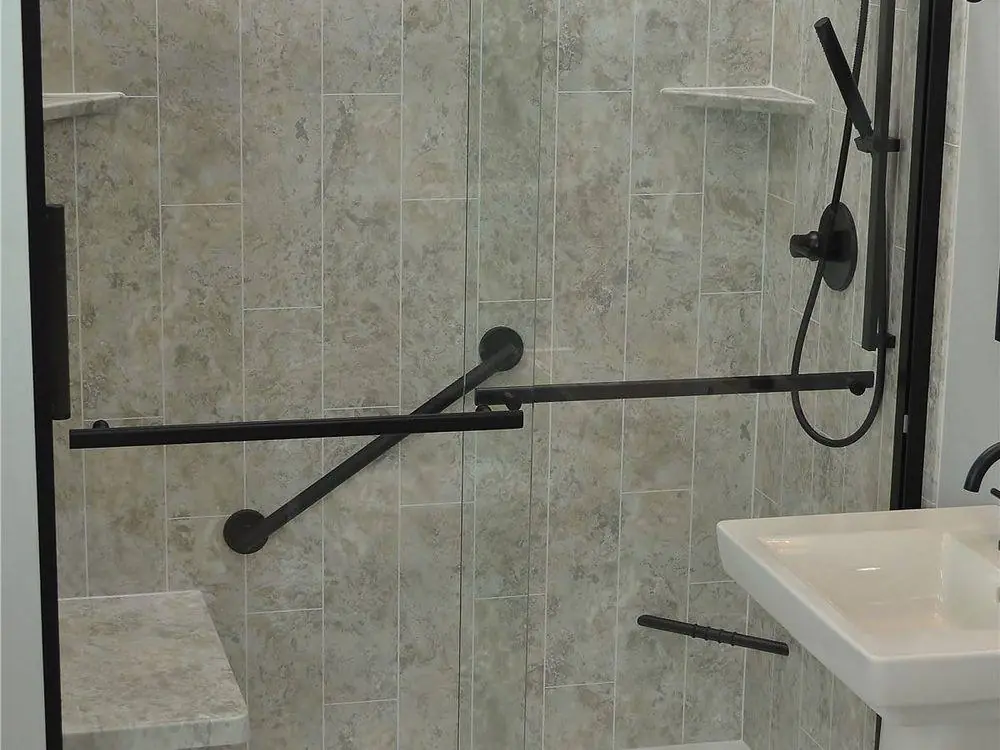 New shower with grey stone look plank walls, a black framed sliding glass door, a grab bar and a bench seat