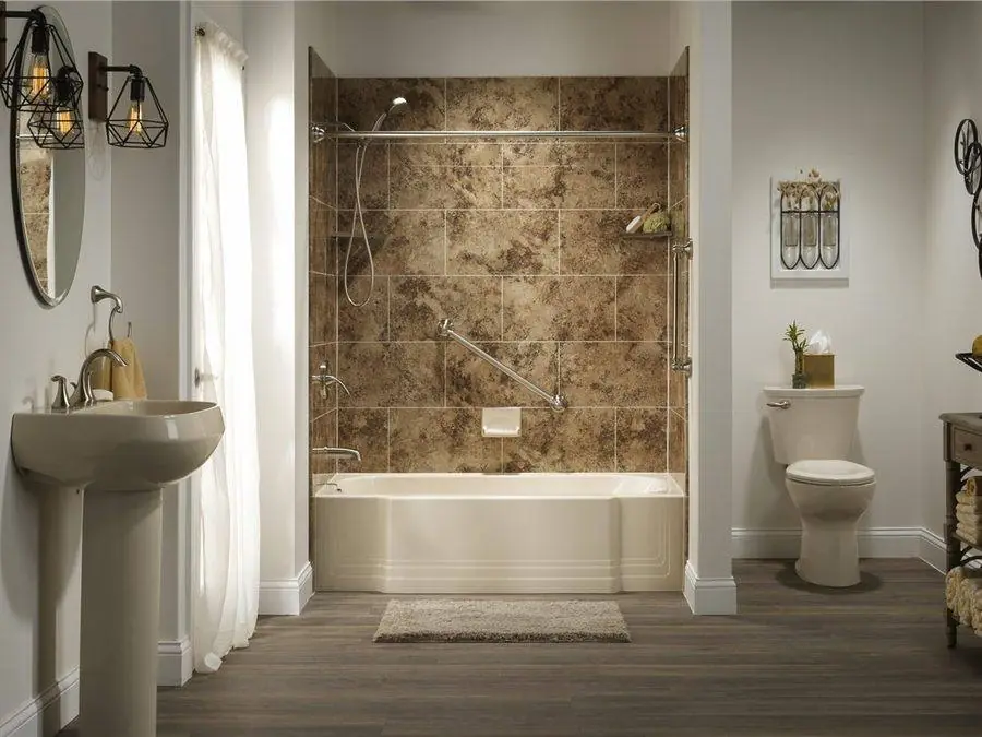 Bathtub with a warm brown stone look surround and a pedestal sink