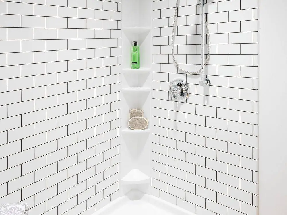 White subway tile look shower walls with corner shelves and a handheld shower on a slide bar