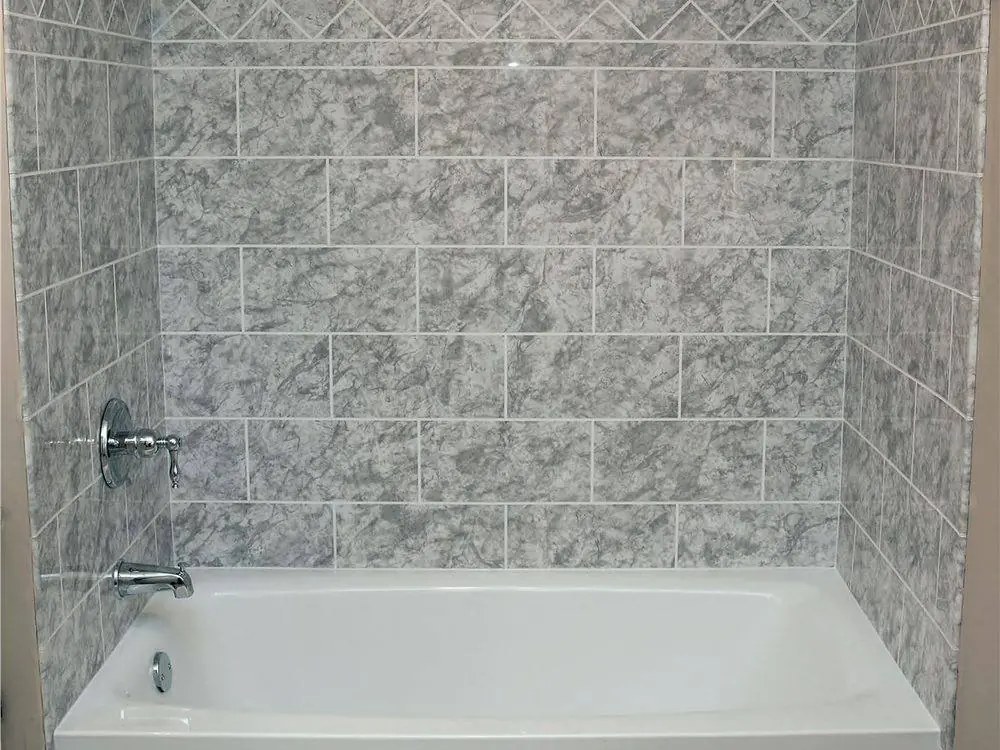 Gray stone look wall surround in a brick pattern around a white bathtub with chrome fixtures