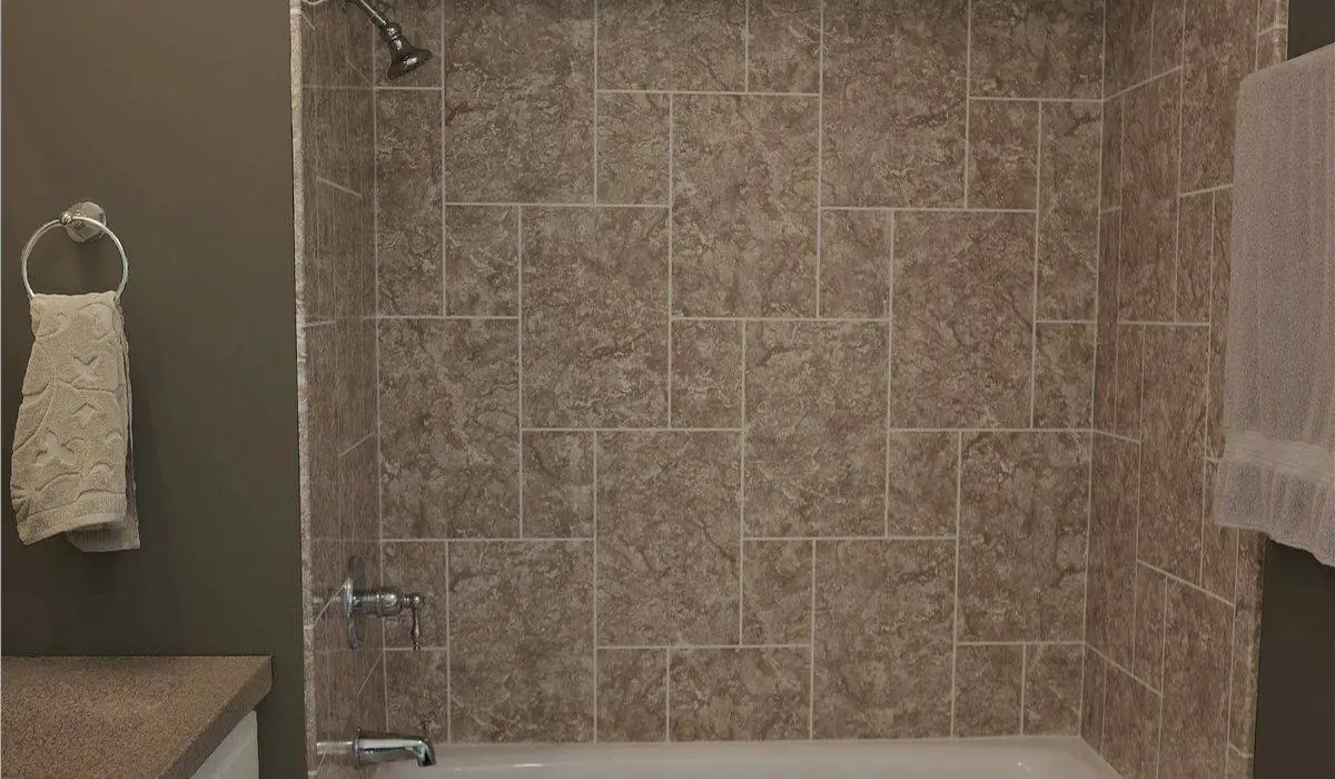 Tan stone look shower wall panels in a large tile pattern above a white tub